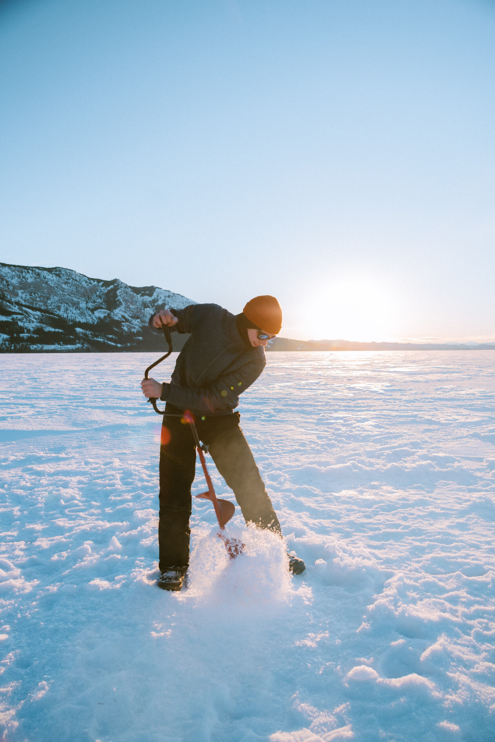 Man ice fishing in snow at sunset