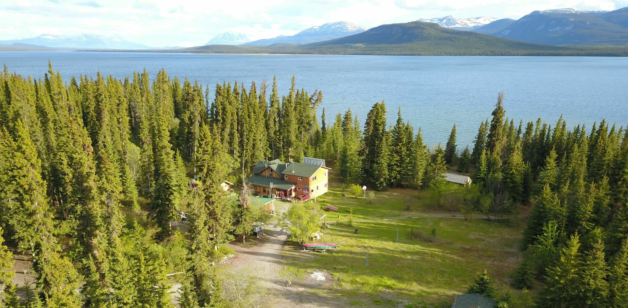 Aerial photo of Little Atlin Lodge showing a secluded lakeside house surrounded by forest and mountains.